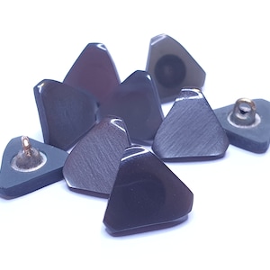Puede incluir: Surtido de siete botones triangulares en tonos grises y negros con detalles en metal dorado. Los botones tienen un acabado liso y brillante.