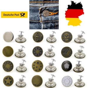 Op de afbeelding: Assortiment van 15 metalen jeansknopen met verschillende ontwerpen, waaronder een kroon, een schedel, sterren en het woord "Jeans". De knopen zijn zilver en brons van kleur en hebben een pen om aan kleding te bevestigen.