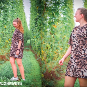 May include: A person wearing a brown and black leopard print dress standing in a field of green plants. The person is smiling and looking down. The plants are tall and have green leaves. The background is a field of green grass.