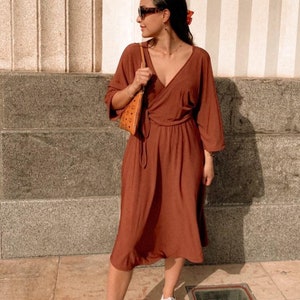 Puede incluir: Un vestido cruzado de color &oacute;xido con cuello en V y mangas tres cuartos. El vestido se combina con zapatillas blancas y un peque&ntilde;o bolso marr&oacute;n. La imagen incluye el texto "NADEA_CREATIVE" y el hashtag "#SEWINGMACHINABERND".