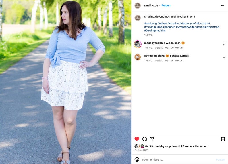 Pu&ograve; includere: Una donna indossa una blusa azzurra annodata in vita e una gonna bianca a strati con un motivo floreale. &Egrave; in piedi su un sentiero lastricato con alberi verdi su entrambi i lati. L'immagine proviene da un post sui social media con il testo "smalino.de Und nochmal in voller Pracht #werbung #n&auml;hen #smalino #derponyhof #lochstrick #melange #Designn&auml;hen #wraptopwalter #miniskirtmanfred #Sewingmachina 151 Wo"