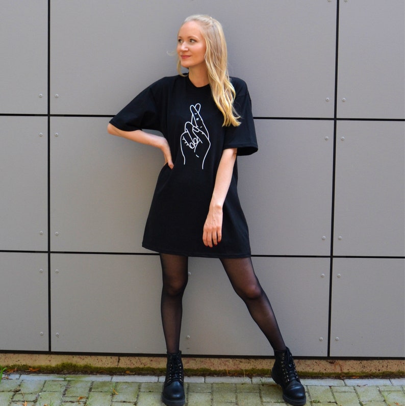 May include: A black oversized t-shirt with a white outline of crossed fingers on the front. The model is wearing black tights and black ankle boots.