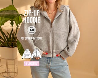 Puede incluir: Una sudadera con capucha gris claro, cierre de cremallera, mangas largas y dos bolsillos delanteros. La imagen incluye el texto ZIP-UP HOODIE, VIDEO TUTORIAL, PDF SEWING PATTERN y 2 LENGHTS, junto a dos bocetos lineales de la sudadera.