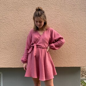 Puede incluir: Un vestido cruzado rosa empolvado con mangas largas y cintur&oacute;n anudado. El vestido tiene una falda acampanada y est&aacute; hecho de una tela texturizada. El texto "BUTFIRSTSEWING" est&aacute; en la parte superior y "#SEWINGMACHINABERND" en la inferior.