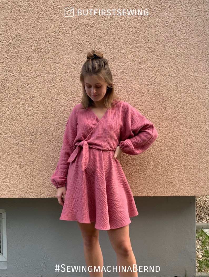 Puede incluir: Un vestido cruzado rosa empolvado con mangas largas y cintur&oacute;n anudado. El vestido tiene una falda acampanada y est&aacute; hecho de una tela texturizada. El texto "BUTFIRSTSEWING" est&aacute; en la parte superior y "#SEWINGMACHINABERND" en la inferior.
