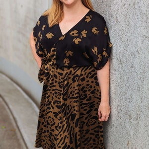 Puede incluir: Vestido estampado en negro y marr&oacute;n con cuello en V y mangas cortas. La parte superior del vestido es negra con un dise&ntilde;o floral dorado, y la parte inferior es marr&oacute;n con estampado de leopardo. El vestido llega a la rodilla.
