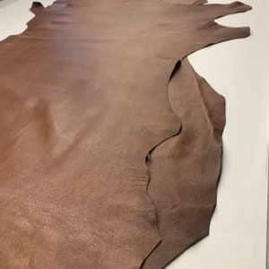 May include: A large piece of brown leather with a textured surface. The leather is folded in half and has a slightly irregular edge.