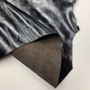 Peut inclure: Une pièce de cuir noir avec une surface brillante et texturée. Le dessous du cuir est de couleur marron foncé. Le cuir est plié, révélant le contraste entre les deux côtés.