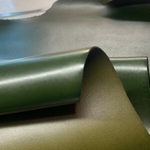 May include: Close-up of a dark green leather hide. The leather is folded over, showing the smooth, shiny surface and the textured underside.