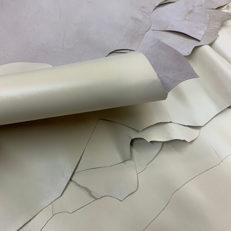 May include: A close-up of a stack of off-white leather pieces. The leather is soft and supple, and it has a slightly textured surface.