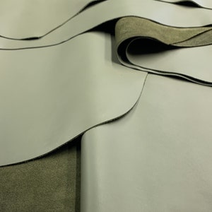 May include: Close-up of two pieces of light gray leather folded over a piece of dark green leather.