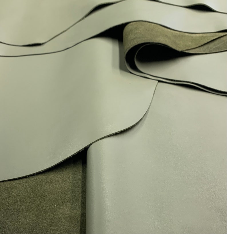 May include: Close-up of two pieces of light gray leather folded over a piece of dark green leather.