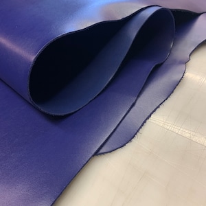 May include: A close-up of a folded piece of dark blue leather. The leather has a smooth, polished finish and is folded in a way that shows the edges.