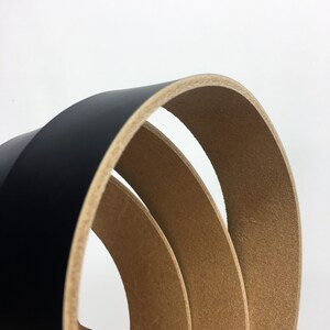 May include: Close-up of three curved black leather belts with a light brown interior. The belts are stacked, revealing the contrasting textures and colours. The background is plain white.