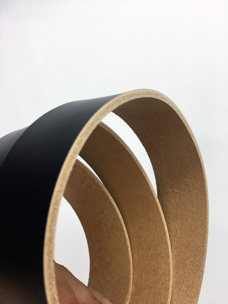 May include: Close-up of three curved black leather belts with a light brown interior. The belts are stacked, revealing the contrasting textures and colours. The background is plain white.