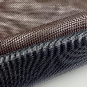 May include: Close-up of three rolls of textured faux leather in shades of brown and navy blue. The material has a woven pattern, creating a basketweave effect. The lighting highlights the sheen of the material.