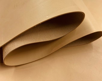 May include: A large, folded sheet of smooth, light tan vegetable-tanned leather. The material features a consistent, matte surface texture on the top side, while the underside reveals a slightly rougher, natural grain characteristic of raw hide.