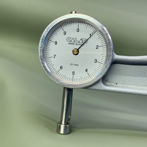 May include: A silver dial gauge with a white face and black markings. The gauge reads 0.1 mm and has the text "CALATI MADE IN ITALY" printed on the face.
