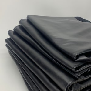 May include: A stack of folded black leather sheets with a smooth, matte finish. The layers are neatly piled, showing the consistent texture and deep black colour of the material. Each sheet is layered to create a structured, uniform appearance.