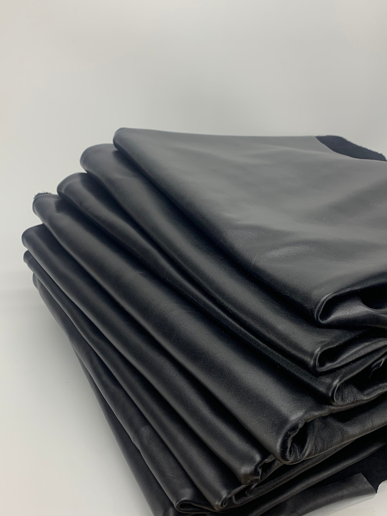 May include: A stack of folded black leather sheets with a smooth, matte finish. The layers are neatly piled, showing the consistent texture and deep black colour of the material. Each sheet is layered to create a structured, uniform appearance.