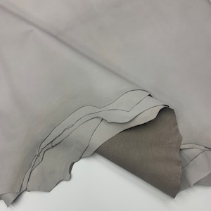 Könnte beinhalten: Ein Stück graues Leder, das in der Mitte gefaltet ist und die Unterseite des Leders zeigt, die eine dunklere graue Farbe hat.