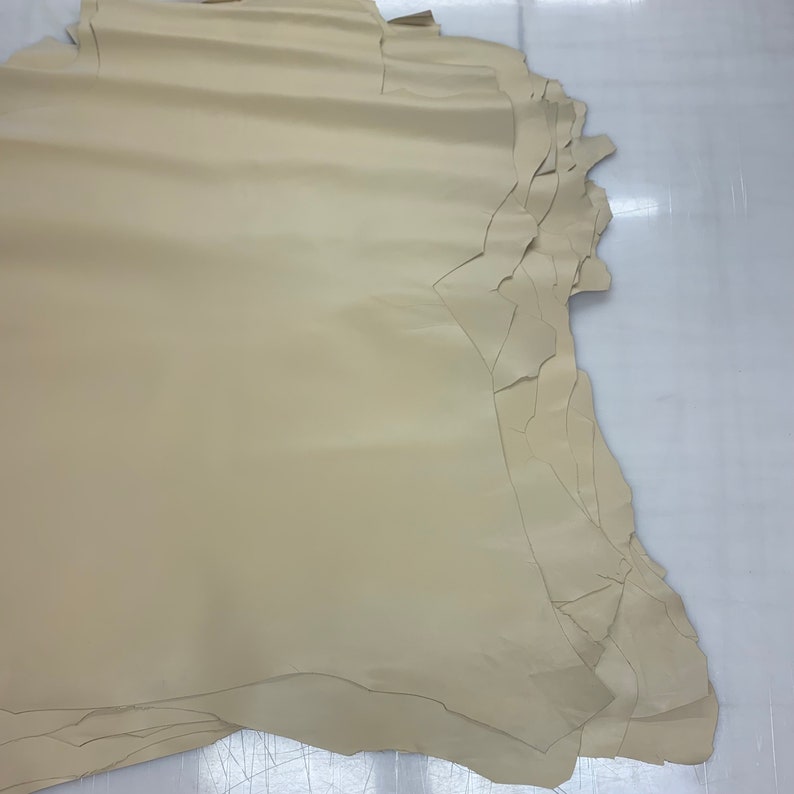 May include: A stack of beige leather hides, each with a slightly different shape and size. The leather is smooth and appears to be of good quality.