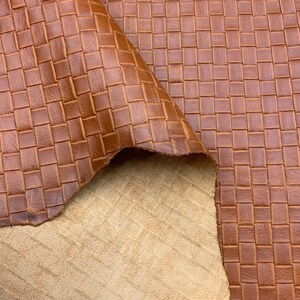 May include: Close-up of a brown leather fabric with a woven pattern. The fabric has a textured surface and a slightly distressed look.