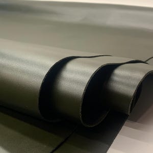 May include: Close-up of a roll of olive green leather. The leather is smooth and has a slight sheen, with visible folds and curves. The edges of the leather are dark, creating a contrast with the lighter surface.