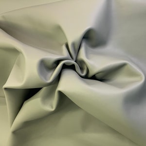 May include: A close-up of a piece of soft, light gray leather fabric. The fabric is folded and draped, showing its texture and drape.