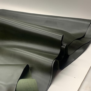 May include: A close-up shot of a dark green leather sheet, folded and layered. The leather has a smooth, matte finish, with subtle variations in tone. The edges of the leather are visible, revealing the thickness and texture of the material.
