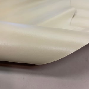 May include: Close-up of a cream-coloured fabric with a textured surface. The fabric is folded over, showing the underside.