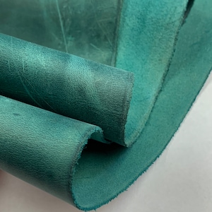 Pode incluir: Close-up de um pedaço de couro teal dobrado com uma superfície texturizada.