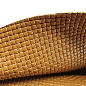 May include: Close-up of a sheet of woven leather in a warm, golden-brown hue. The texture is a tight, basketweave pattern, with a slight sheen. The leather is folded, revealing the underside.