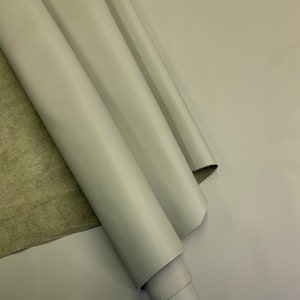 May include: A roll of light gray leather fabric. The leather is smooth and has a slight sheen.