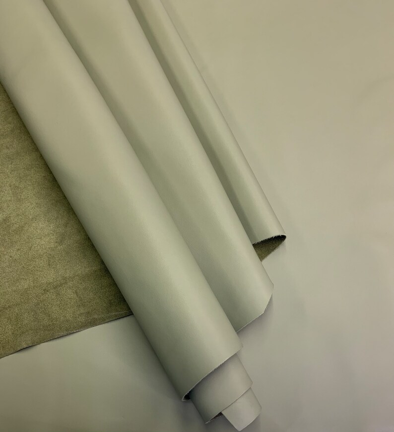 May include: A roll of light gray leather fabric. The leather is smooth and has a slight sheen.