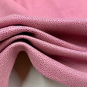 May include: Close-up of pink leather fabric with a textured, dotted pattern. The fabric is folded, revealing the texture and color variations. The material has a smooth, soft appearance, suitable for various crafting projects.
