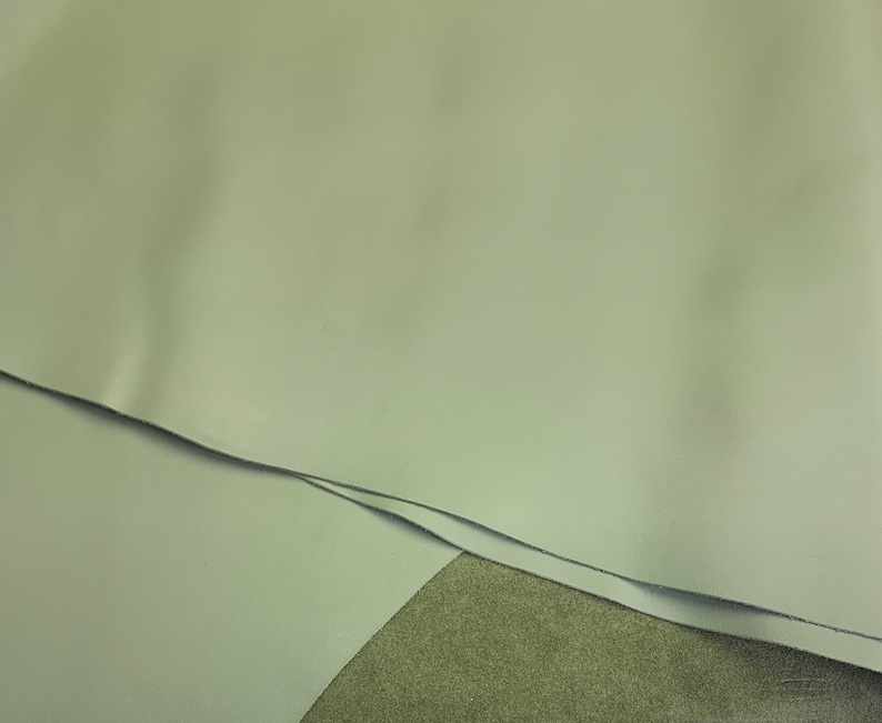 May include: Close-up of a light gray leather material. The leather is folded over itself, showing the smooth texture.
