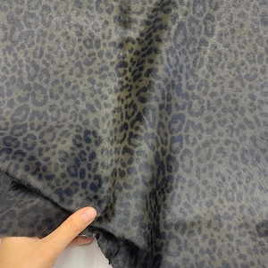 May include: Close-up of a dark green fabric with a black leopard print pattern. The fabric has a soft, fuzzy texture.