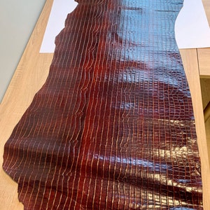 May include: A large piece of brown alligator leather with a glossy finish. The leather has a distinct pattern of scales.