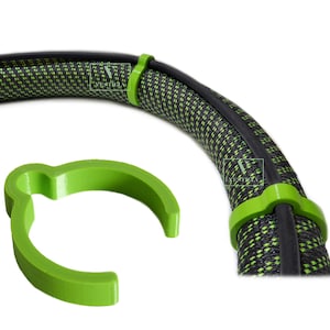 May include: A close-up of a black and green cable with green clips. The cable has a woven pattern and is held in place by bright green plastic clips. One clip is separate from the cable, showing its curved design.