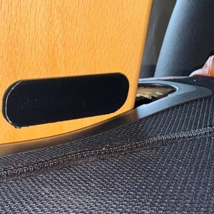May include: A light-colored wooden furniture leg with a black rectangular accent. A red rectangular object is visible near the base. The leg is set against a black textured surface.