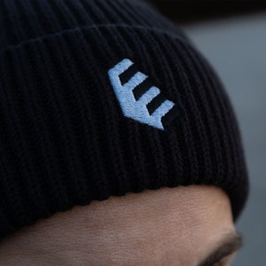 Könnte beinhalten: Schwarze Strickmütze mit einem weißen gestickten Logo eines stilisierten Buchstabens "E" mit drei Linien.