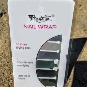 May include: A white package with a black and pink logo that says "野蛮女友Ⓡ NAIL WRAP". The package shows a set of nail wraps in shades of gray and green. The text on the package says "no more drying time", "0 drbordement smudging", and "lasts up to 7 days".