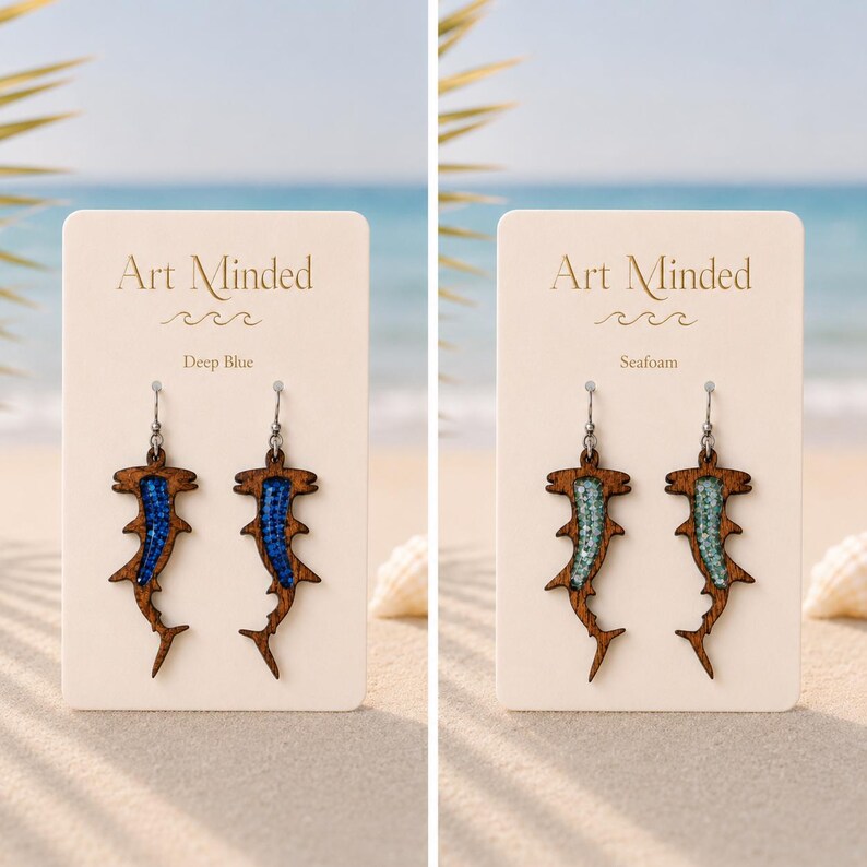 May include: Two pairs of hammerhead shark earrings on display cards. One pair features dark wood with deep blue inlay, the other features dark wood with seafoam green inlay. Each earring has a silver-toned metal hook and a cutout shark silhouette.