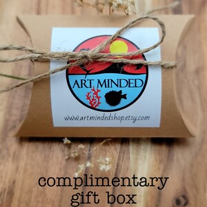 May include: A brown cardboard pillow-style gift box tied with natural twine. A circular sticker features a red and blue design with a yellow sun, a black fish, and red coral, with the text ART MINDED and www.artmindedshop.etsy.com printed below.