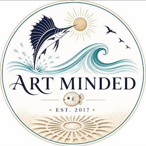 May include: A circular logo featuring a dark blue sailfish leaping from a teal ocean wave toward a golden sun. The text ART MINDED is centered above a small pufferfish illustration and the text EST. 2017, with a sand pattern at the bottom.