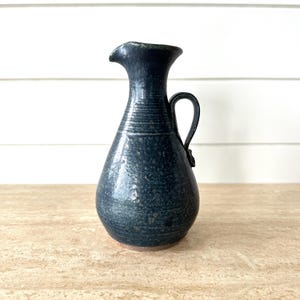 May include: A white ceramic mug with a black handle and the text "But first, coffee" in a handwritten style. The mug is on a white surface. The mug is approximately 10 cm tall.