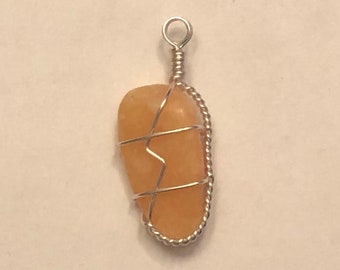 May include: A wire-wrapped pendant featuring a light orange stone. The stone is wrapped in silver wire, creating a delicate and intricate design.
