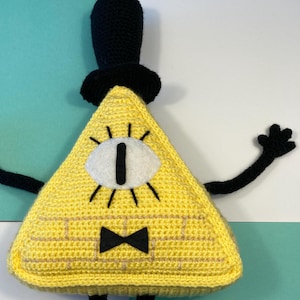 May include: A yellow crocheted triangle plush toy with a black top hat, a white eye, and a black bow tie. The toy has black crocheted arms and legs.