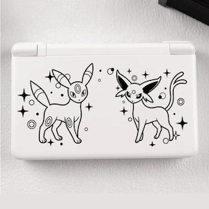 Könnte beinhalten: Weiße Nintendo DS Lite Konsole mit schwarzen Strichzeichnungen von zwei stilisierten Kreaturen mit großen Ohren und Schwänzen, umgeben von Sternen und Kreisen. Die Konsole ist geschlossen und hat eine glatte Oberfläche.